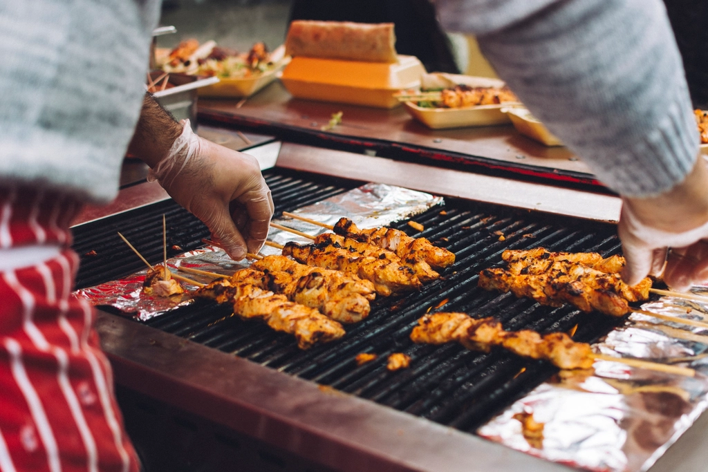 Kipspiesjes liggen naast elkaar op een grillrooster achter een toonbank.