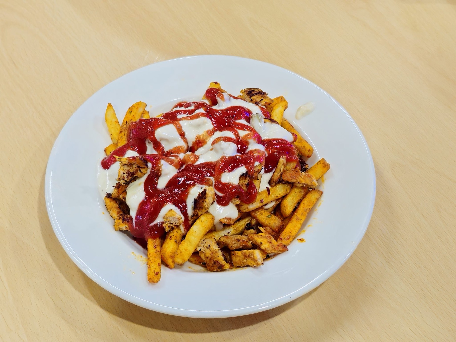 Bord met friet, gegrilde stukjes kip, witte saus en tomatensaus.